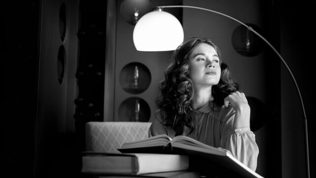девушка, книга, библиотека, чтение, взгляд, улыбка, чб, черно белый, стол, свет, лампа, книги